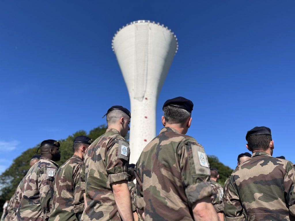 Les militaires du 1er régiment d'artillerie, en rangs, font face au nouveau mur d'escalade installé sur le château d'eau de la base de Bourogne. | © Le Trois - H.G.
